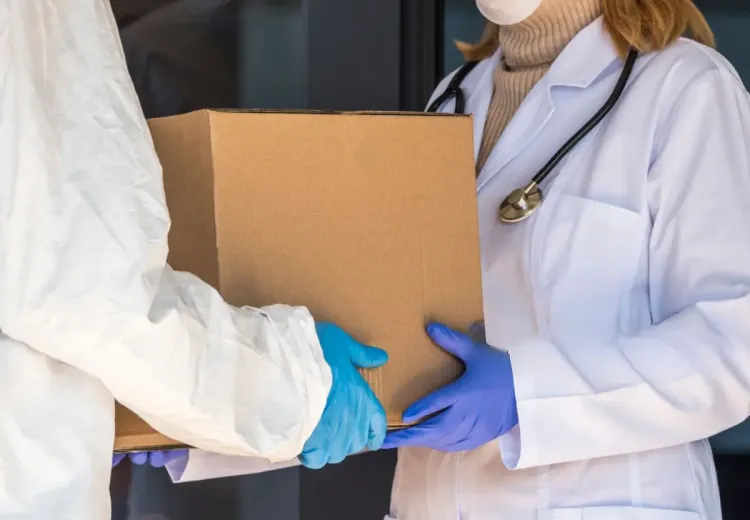 Une personne en combinaison de protection reçoit une boîte de médicaments à un médecin à l’entrée de l’hôpital 