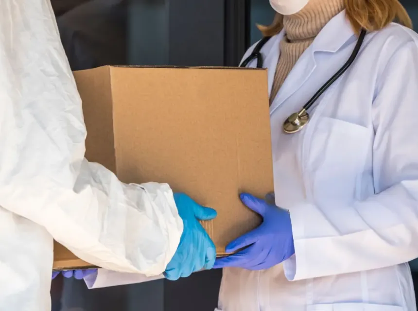 Une personne en combinaison de protection reçoit une boîte de médicaments à un médecin à l’entrée de l’hôpital 